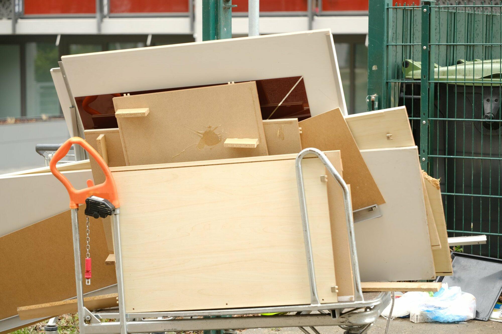 Entsorgte Möbelteile auf Wagen neben Müllcontainern